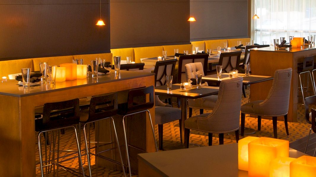 A stylish, warmly lit restaurant with wooden tables, modern chairs, and glowing candle-like lights creating an intimate dining vibe.