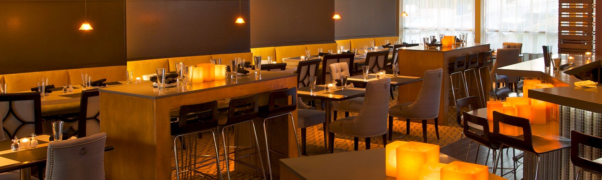 A stylish, warmly lit restaurant with wooden tables, modern chairs, and glowing candle-like lights creating an intimate dining vibe.