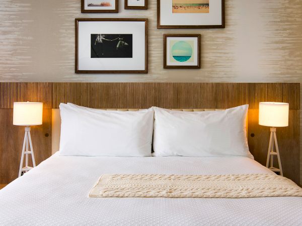 A modern hotel bedroom with a neatly made bed, two table lamps, and framed wall art above the headboard.