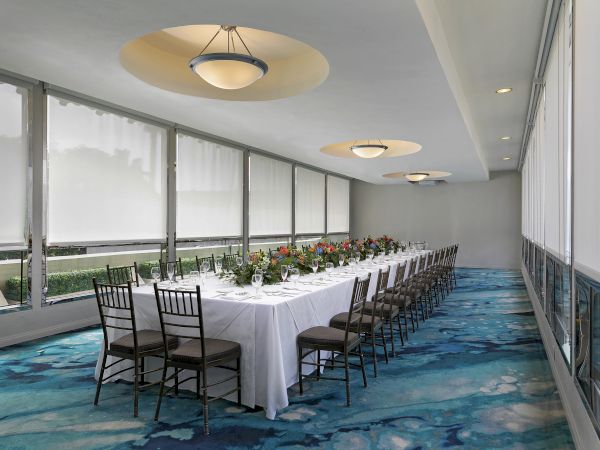 Banquet room set for an event: long tables with chairs, flower centerpieces, and ceiling pendant lights.