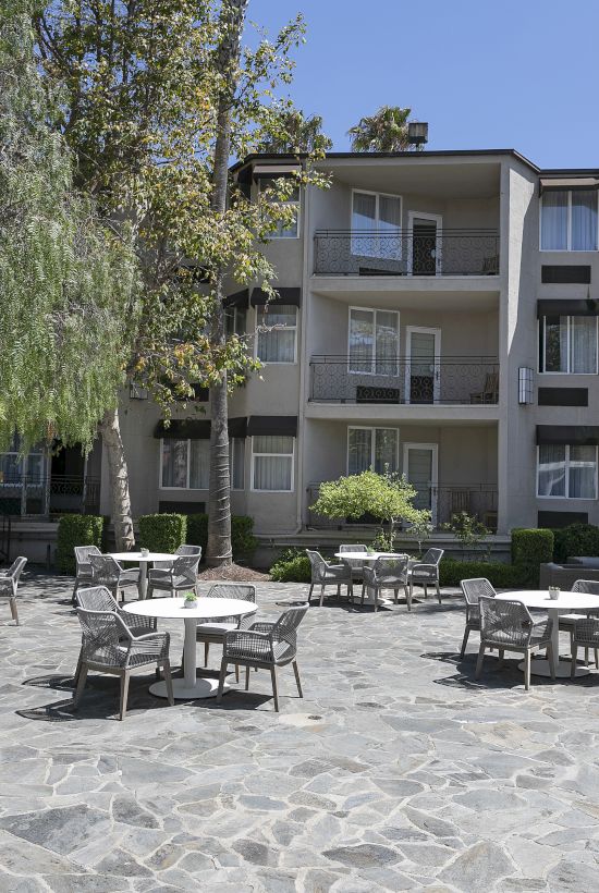 Outdoor patio courtyard with stone paving, lounge chairs and tables, and a white multi-story apartment building with balconies.