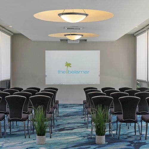 Modern meeting room with many chairs, projector screen, large blinds, and circular ceiling lights.