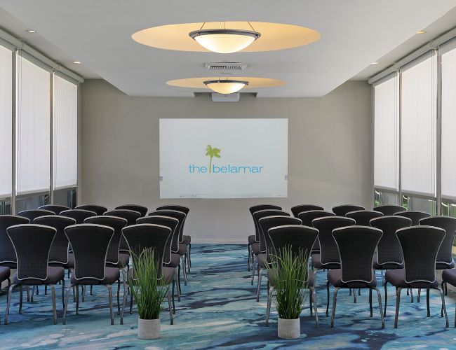 Modern meeting room with many chairs, projector screen, large blinds, and circular ceiling lights.