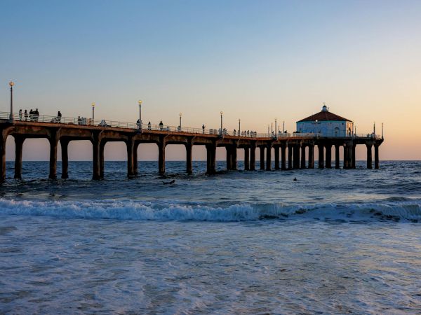 Sunset at a seaside pier with people strolling on the walkway and waves rolling beneath.