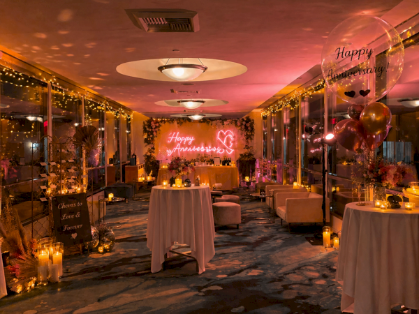A warmly lit indoor celebration corridor with candles, balloons, and a glowing &ldquo;Happy Anniversary&rdquo; backdrop.