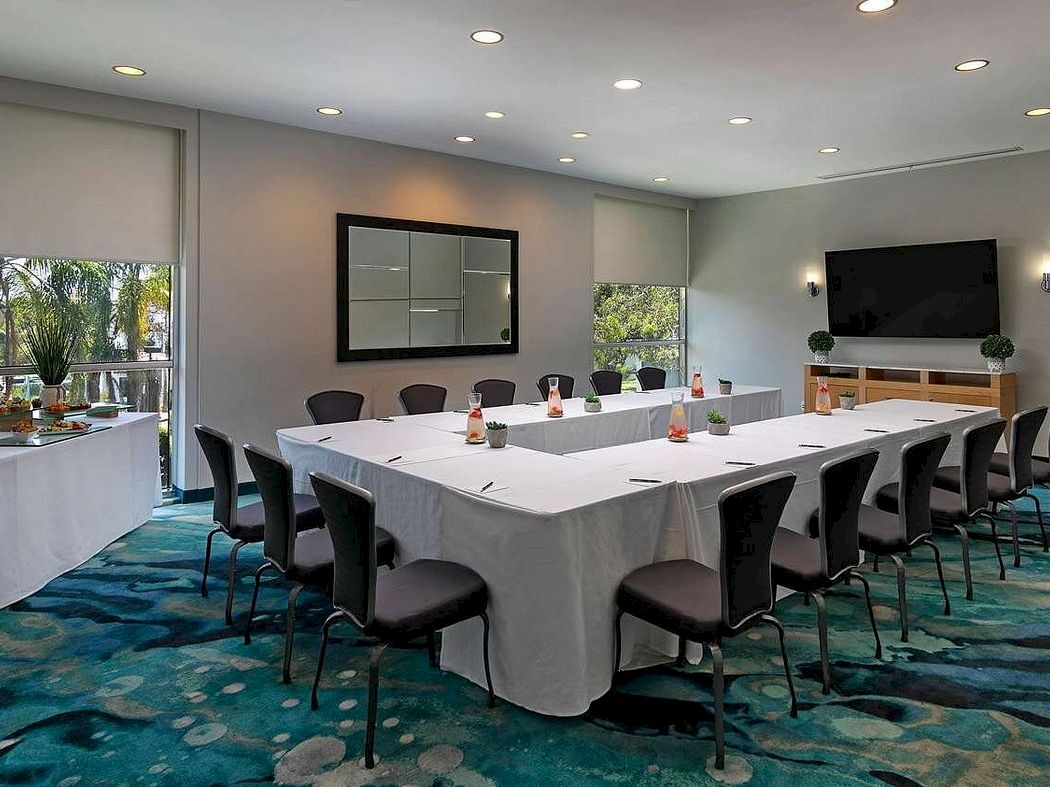 A modern conference room with a long white banquet table, chairs, and TVs, set on a blue patterned carpet.