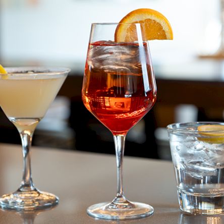A bar table with four colorful cocktails&mdash;red, pale, amber with orange slice, and a blue drink&mdash;each garnished with citrus.