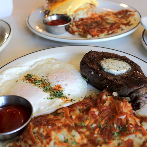 Plates of steak with a sunny-side egg, pizza, and a side salad with sauces, all ready to eat.