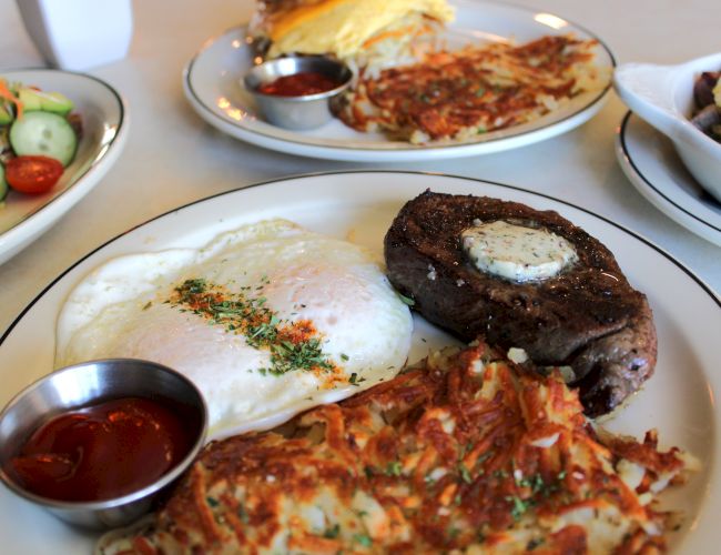 Plates of steak with a sunny-side egg, pizza, and a side salad with sauces, all ready to eat.