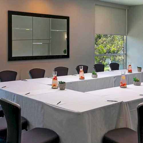 A modern conference room with a long banquet table, microphones, drinks, and a buffet spread by large windows, ready for a meeting.
