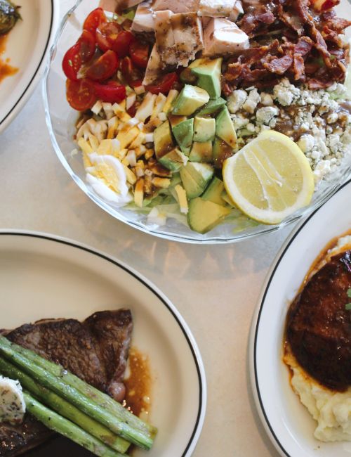 Plates of steak with roasted vegetables, a hearty chopped salad with avocado, tomato, feta, lemon, plus asparagus and fries, too.
